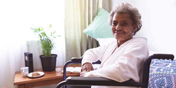 Portrait of happy mixed race senior woman sitting in wheelchair while looking at camera at nursing home